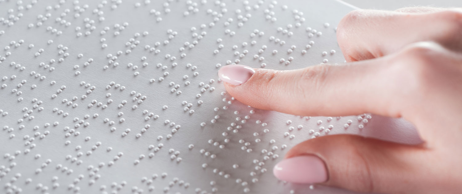 Die rechte Hand von einer Frau berührt auf einer Metallplatte unterschiedliche Buchstaben. Die Buchstabend sind im Braille-Alphabet. Blinde Menschen können mit den Braille-Zeichen Texte lesen.