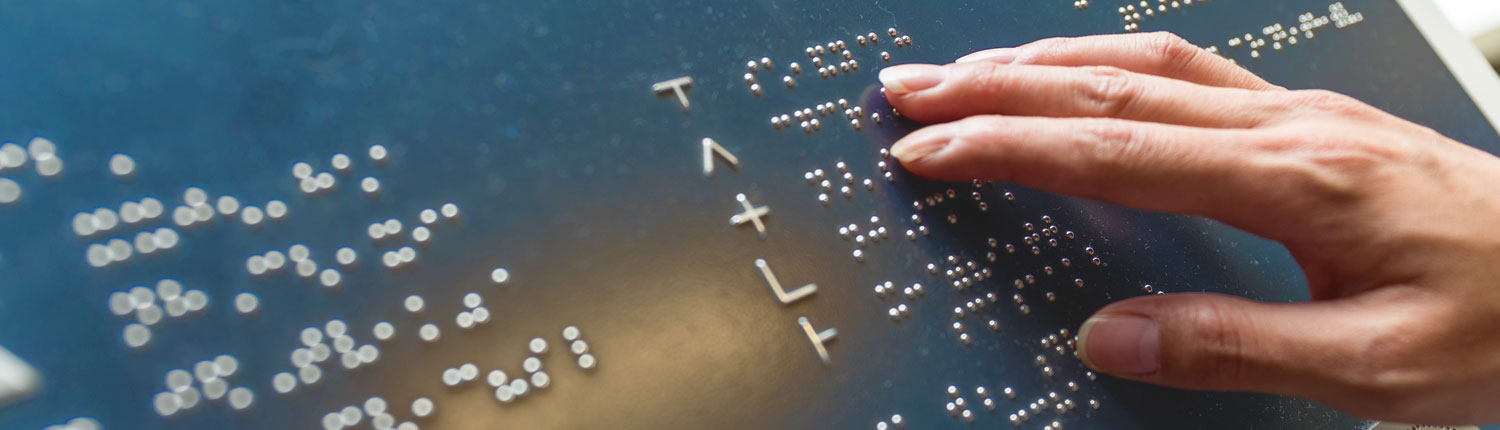 Die rechte Hand von einer Frau berührt auf einer Metallplatte unterschiedliche Buchstaben. Die Buchstabend sind im Braille-Alphabet. Blinde Menschen können mit den Braille-Zeichen Texte lesen .