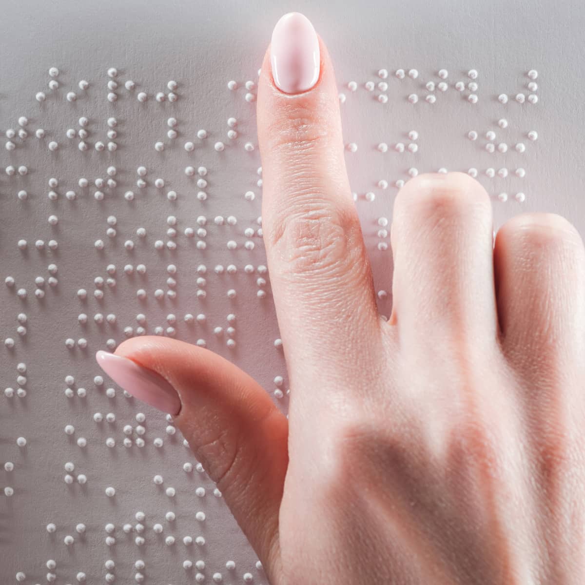 Die rechte Hand von einer Frau berührt auf einer Metallplatte unterschiedliche Buchstaben. Die Buchstabend sind im Braille-Alphabet. Blinde Menschen können mit den Braille-Zeichen Texte lesen.