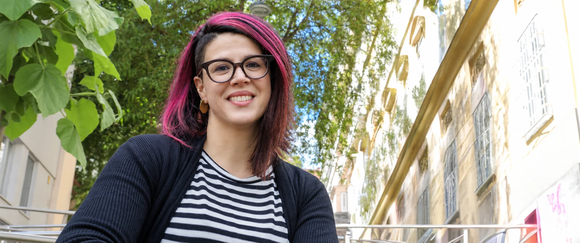 Barrierefreie Kommunikation: Erfolgreiche Kommunikation durch Expertise und Weitblick Eine Frau mit rosa-schwarzen Haaren und Seitenscheitel, brauner runder Brille und goldenen Ohrringen lächelt in die Kamera: Es ist Verena Brinda